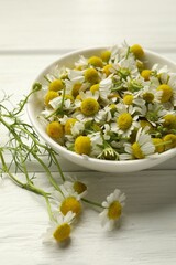 Fresh chamomile flowers and bowl on white wooden table, closeup