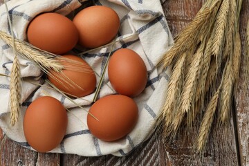 Raw eggs, fabric and spikes of wheat on wooden table, flat lay