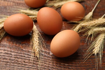 Raw eggs and spikes of wheat on wooden table, closeup