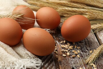 Raw eggs, fabric and spikes of wheat on wooden table, closeup