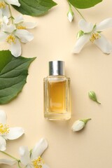 Bottle of perfume, beautiful jasmine flowers and green leaves on beige background, flat lay