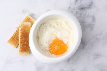 Half-boiled egg in bowl and toasted bread on white marble table, top view. Traditional asian breakfast