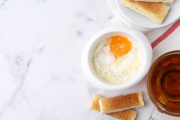 Half-boiled egg in bowl, tea and toasted bread on white marble table, flat lay. Traditional asian breakfast