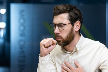 Close-up photo of a young male office worker in eyeglasses and with a beard who is in the office,...