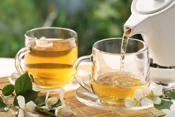 Pouring tasty jasmine tea into cup on white wooden table, closeup