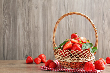 Delicious ripe strawberries in wicker basket on wooden table, space for text