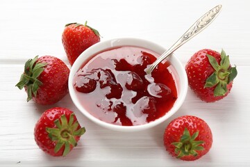 Tasty strawberry jam in bowl and fresh berries on white wooden table, closeup