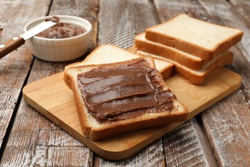 Sandwiches with chocolate butter and knife on wooden table, closeup