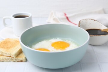 Traditional asian breakfast with half-boiled eggs in bowl, soy sauce, bread and coffee on white tiled table, closeup