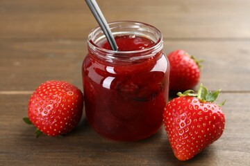 Tasty homemade strawberry jam in glass jar and berries on wooden table, closeup