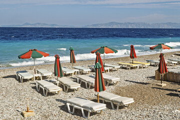 sand beach with orange deck chairs and umbrellas arranged in rows along a pebble beach and the sea...