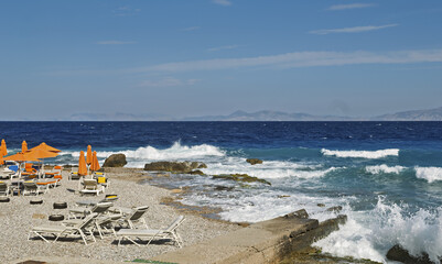 sand beach with orange deck chairs and umbrellas arranged in rows along a pebble beach and the sea...