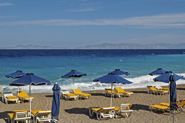 sand beach with blue deck chairs and umbrellas arranged in rows along the sea turquoise in Rhodes,...