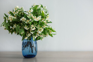 Beautiful jasmine flowers in vase on table indoors, space for text