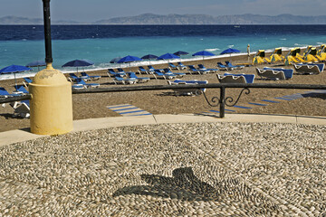 sand beach with blue deck chairs and umbrellas arranged in rows along the sea turquoise in Rhodes,...