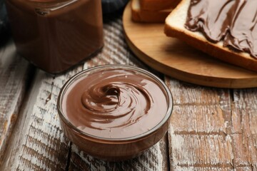 Tasty chocolate butter and slice of bread on wooden table, closeup