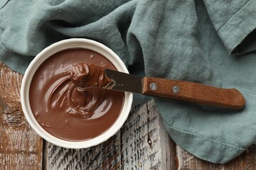Tasty chocolate butter in bowl and knife on wooden table, top view