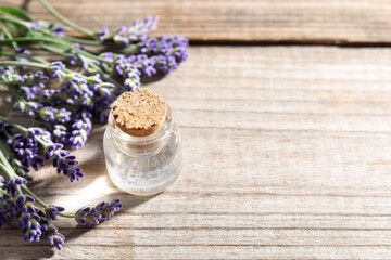 Natural essential oil and lavender flowers on wooden table, closeup. Space for text