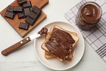 Slices of bread with tasty chocolate butter and knife on white marble table, flat lay