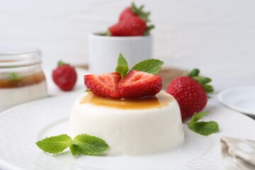 Tasty panna cotta with caramel, strawberries and mint on table, closeup