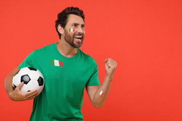 Excited fan with flags of Italy on his body and t-shirt holding soccer ball against red background....