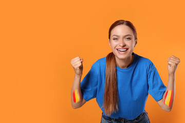 Excited fan with colors matching Spain flag painted on her arms against orange background. Space...