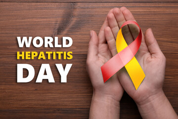 28th july World Hepatitis Day. Woman holding yellow-red awareness ribbon on wooden background, top view