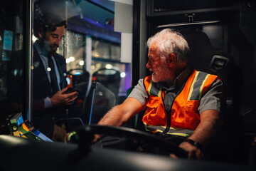 Bus driver wearing safety vest talking to businessman at night