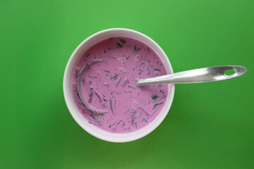Bowl of cold pink beet soup with ladle on green background