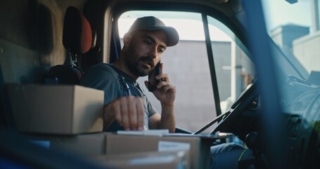 Professional Delivery Truck Driver in Car Talking by Phone with Customer, Filling Out Papers, Using...