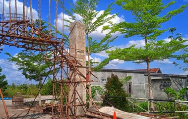 Wooden frame structure at a construction site with a wide cloudy sky and bright sun behind it.