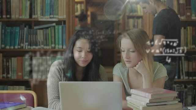 Two students typing, pointing on laptop in library, floating math formulas guiding study session