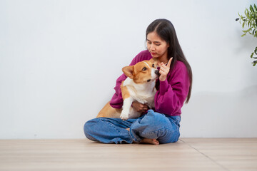 Asian young woman sits on the floor beside her sofa, gently stroking her Corgi dog head relax at...