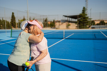 Senior women players hugging after paddle tennis match on blue court