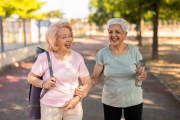 Two senior women walking and smiling after yoga class in the park