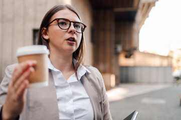 Businesswoman walking and talking on phone holding coffee and notebook