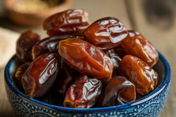 Macro photo of ripe brown dates in a textured blue ceramic bowl showing glossy skin and natural surface imperfections in soft light