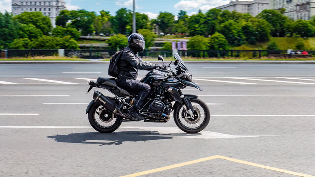 Side view of man in helmet riding black BMW motorbike on city road