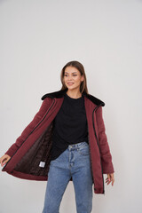 Smiling woman in a maroon jacket with a black collar, open over a black shirt and blue jeans,...