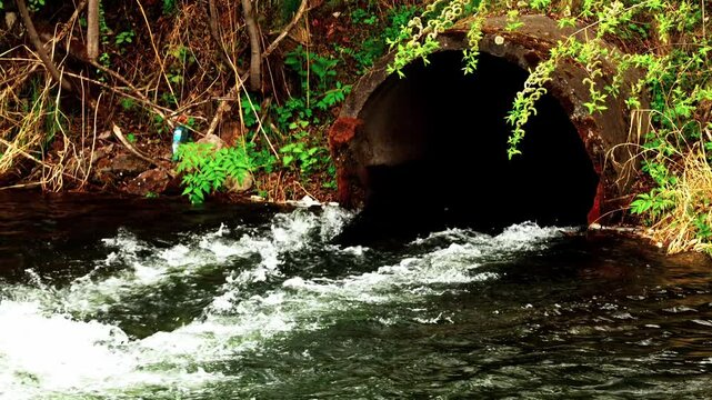 Pipe from underground with waste water, a stream of water with a large sida flows out of the pipe