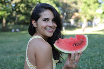 Gorgeous Hispanic woman eating watermelon in the park 