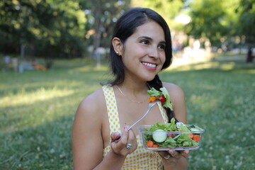 Beautiful Hispanic woman eating a healthy salad in the park 
