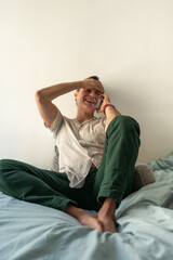 Man laughing while talking on the phone sitting on bed