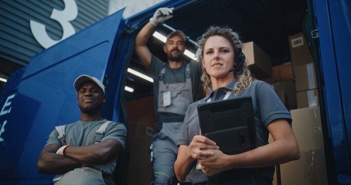 Outside of Logistics Distribution Warehouse: Team of Diverse Workers Standing near Delivery Truck Full of Cardboard Boxes with Online Orders, Looking at Camera. Female Manager Holding Digital Tablet.
