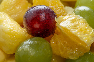 juicy fruit pieces pile with water drops, red grape on pineapple cube, orange in back. fresh fruit salad background head on, close up