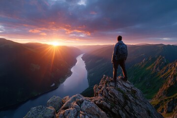 Man standing on a mountain peak overlooking a river at sunset in a scenic landscape