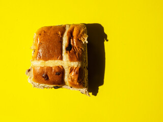 Fine cross bun on warm yellow background, hard lighting, Tasty bakery product. Popular traditional...