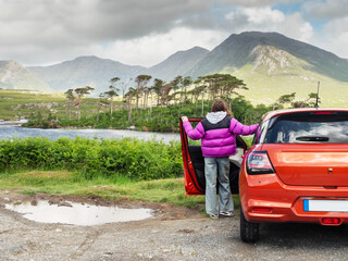 Young teenager girl standing by small red sport car and enjoys view of Twelve pines island and...