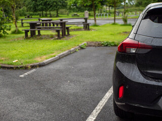 Black family car parked in a parking lot of a park with barbecue or dining area, selective focus....