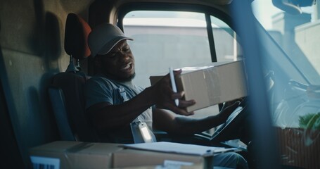 African American Delivery Truck Driver in Car Talking by Mobile Phone with Customer, Filling Out...